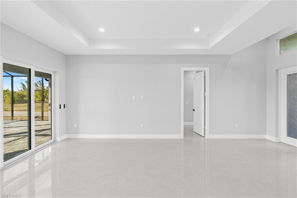 Empty room with finished concrete flooring, a tray ceiling, and recessed lighting