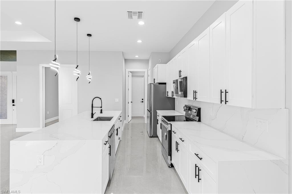 Kitchen featuring light stone counters, appliances with stainless steel finishes, decorative light fixtures, a spacious island, and recessed lighting