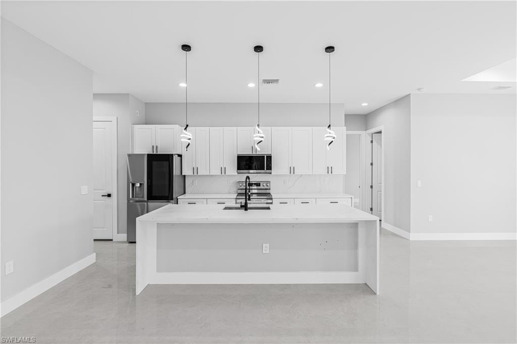 Kitchen with light stone countertops, stainless steel appliances, an island with sink, white cabinetry, and pendant lighting