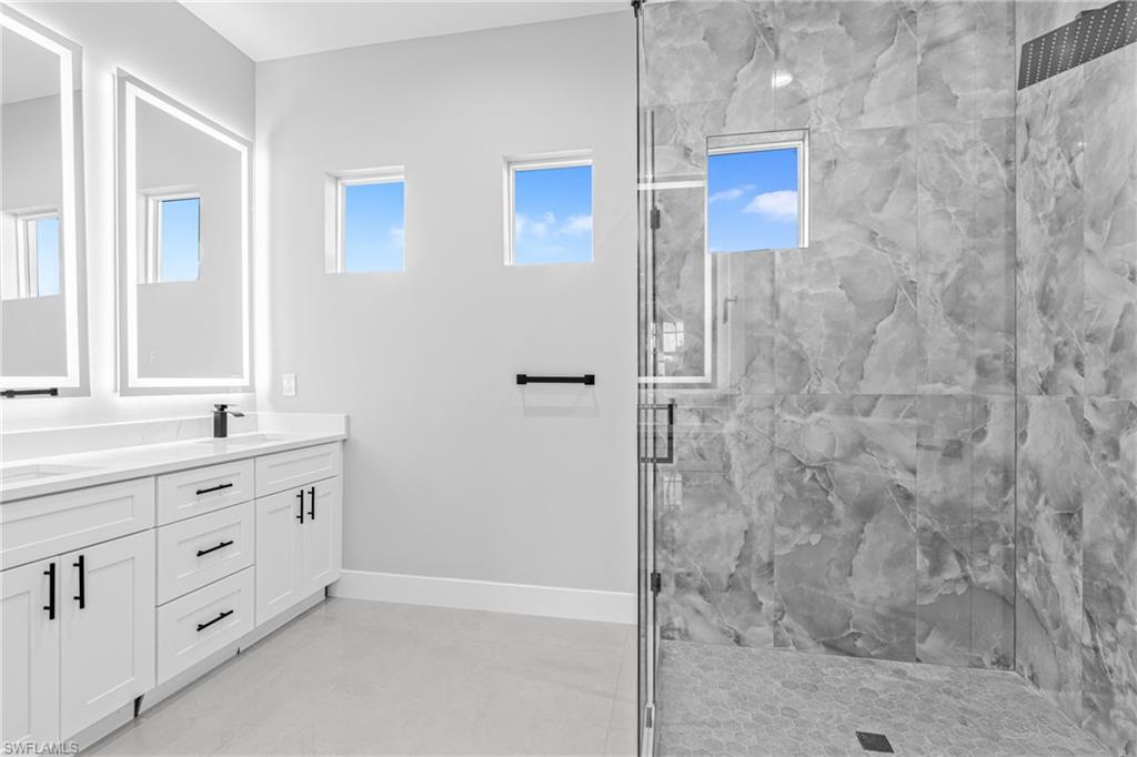 Full bathroom featuring double vanity, a marble finish shower, and plenty of natural light