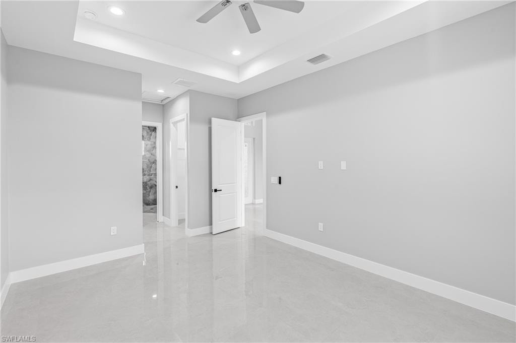 Unfurnished bedroom with a raised ceiling, recessed lighting, ceiling fan, and connected bathroom