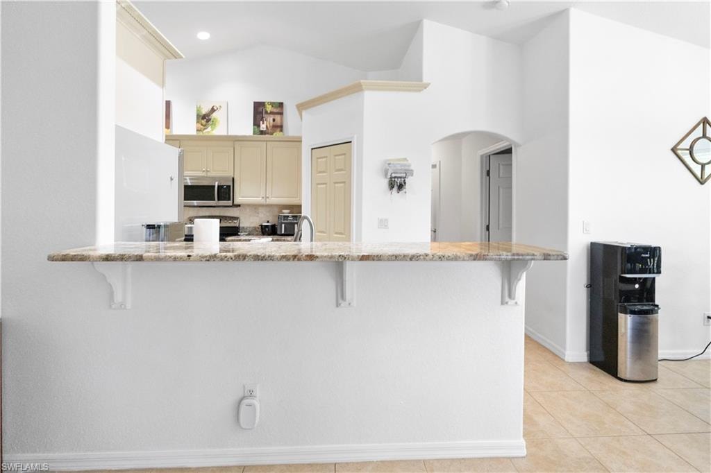 Kitchen with a breakfast bar, arched walkways, cream cabinetry, light stone counters, and stainless steel appliances