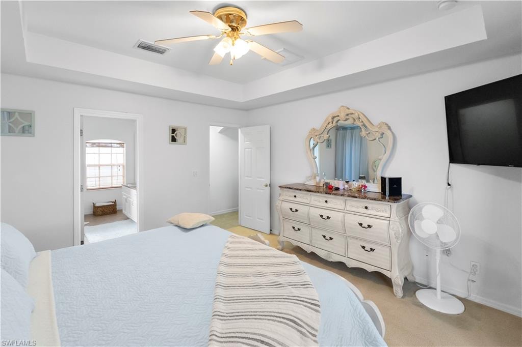 Bedroom with a tray ceiling, a ceiling fan, and connected bathroom