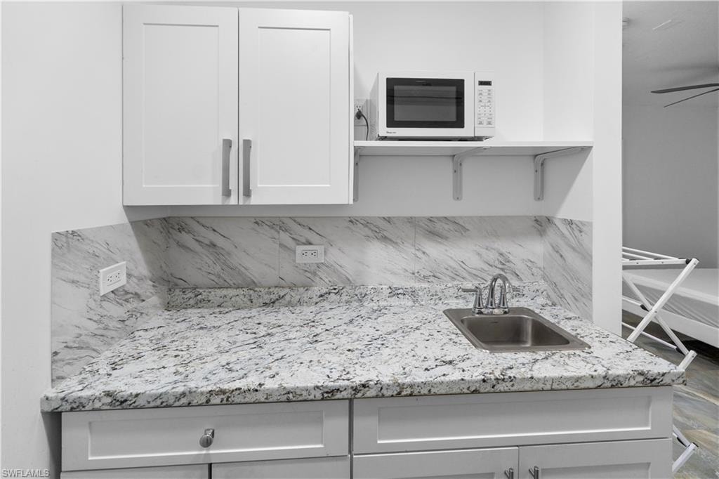 Kitchen featuring white microwave, white cabinetry, light stone counters, tasteful backsplash, and a ceiling fan