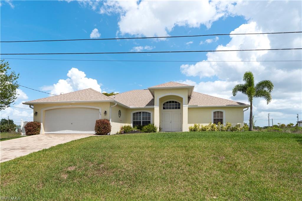 View of front facade with a front yard, stucco siding, a garage, and driveway