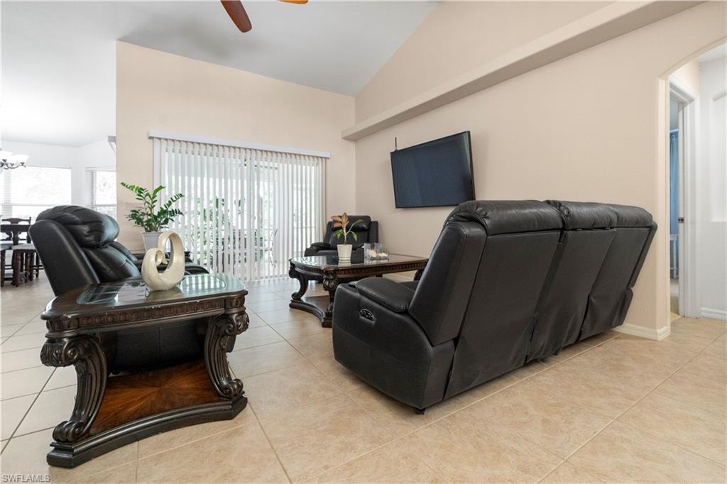 Living room featuring arched walkways, vaulted ceiling, ceiling fan, light tile patterned floors, and a chandelier