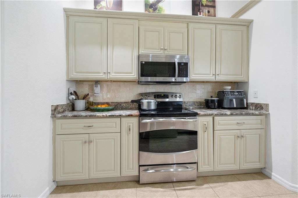 Kitchen with cream cabinetry, stainless steel appliances, and decorative backsplash