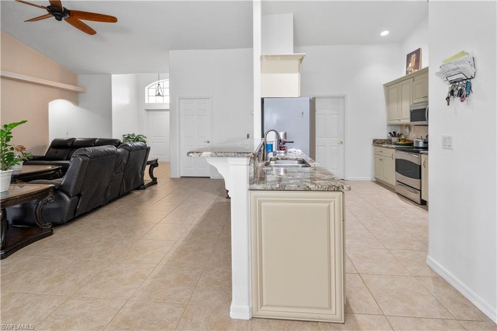 Kitchen featuring cream cabinets, open floor plan, a ceiling fan, light stone counters, and stainless steel appliances