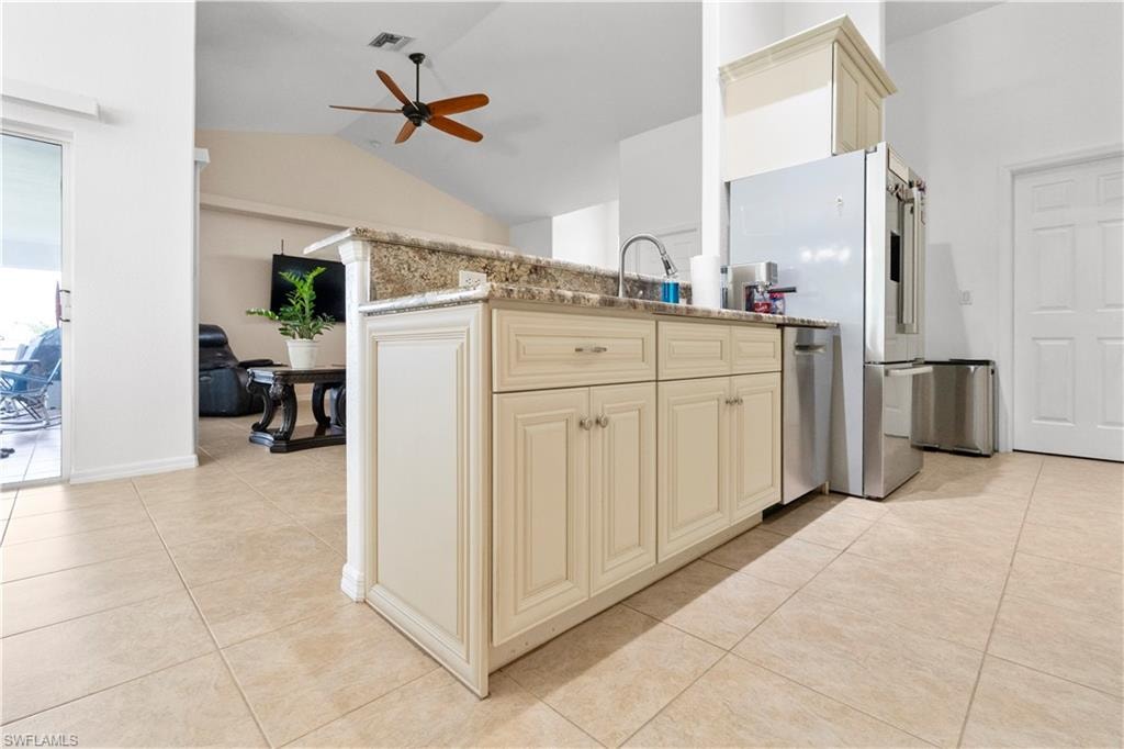 Kitchen with cream cabinetry, ceiling fan, light tile patterned floors, stainless steel appliances, and lofted ceiling