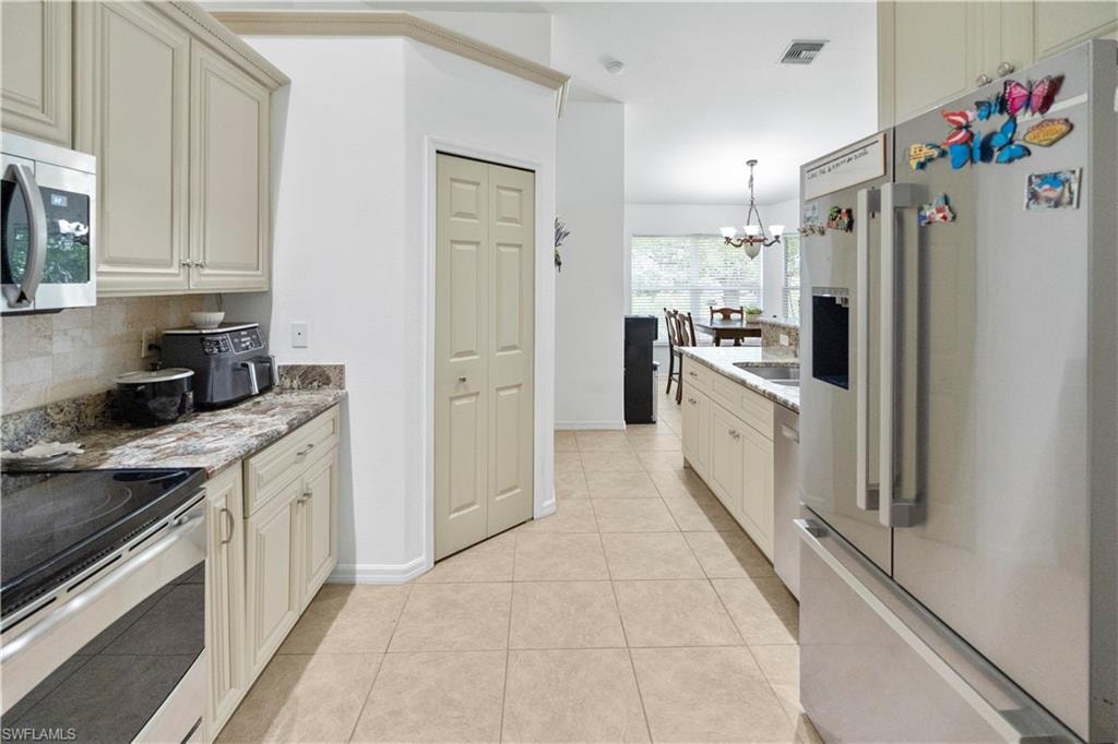 Kitchen with stainless steel appliances, light stone counters, cream cabinetry, light tile patterned floors, and decorative backsplash