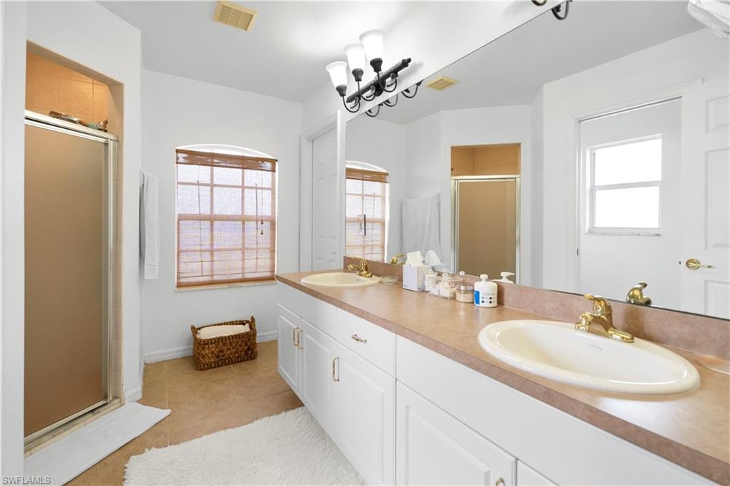 Full bath featuring a stall shower, double vanity, and light tile patterned floors