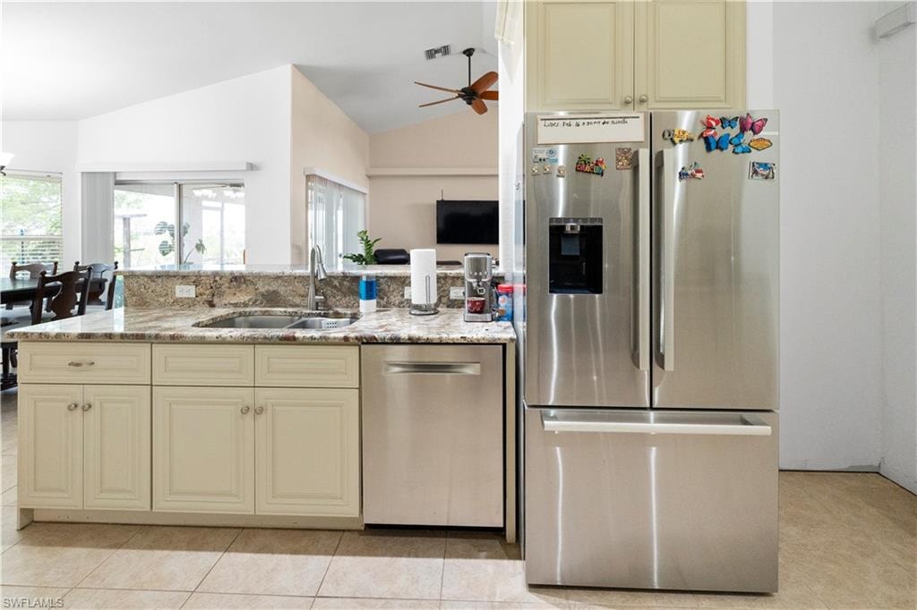 Kitchen with cream cabinetry, stainless steel appliances, a ceiling fan, light stone counters, and open floor plan