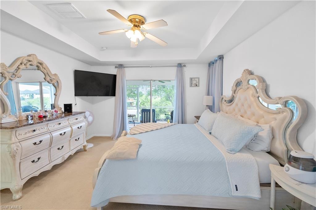 Bedroom featuring a raised ceiling, access to exterior, light colored carpet, and a ceiling fan