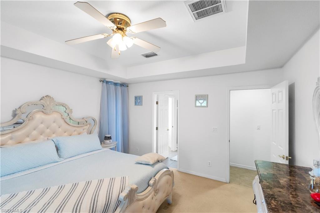 Bedroom featuring light colored carpet, a tray ceiling, and a ceiling fan