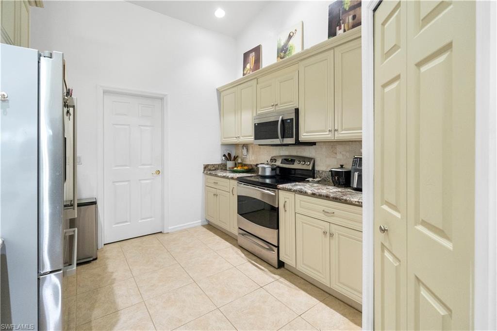 Kitchen with cream cabinetry, stainless steel appliances, backsplash, light tile patterned flooring, and recessed lighting