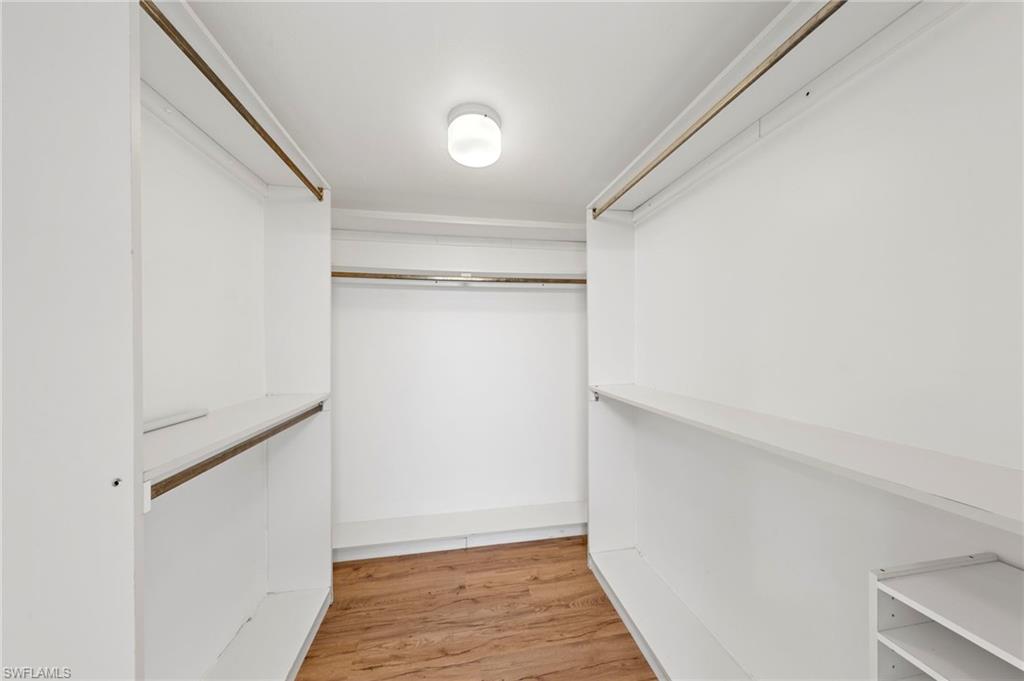 Walk-in closet featuring white built-in shelving, hanging rods, and wood-finish flooring