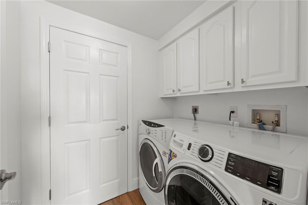 Dedicated laundry area featuring white upper cabinetry, a paneled door, and wood-finish flooring