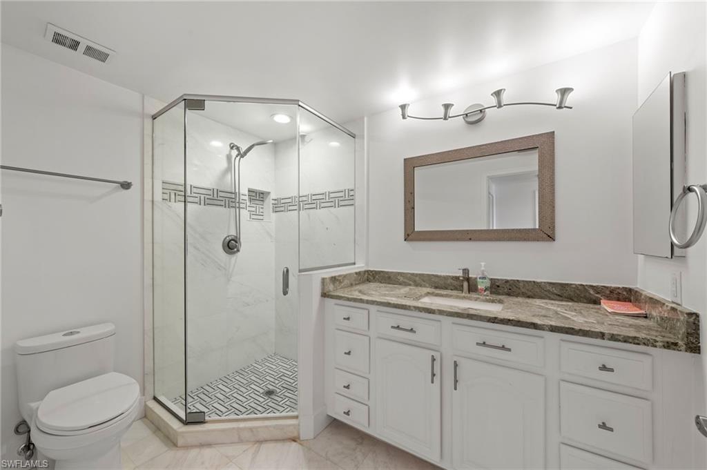 Bathroom featuring a glass-enclosed shower with tiled accents, a white vanity with a stone countertop and integrated sink, a framed mirror, and recessed lighting