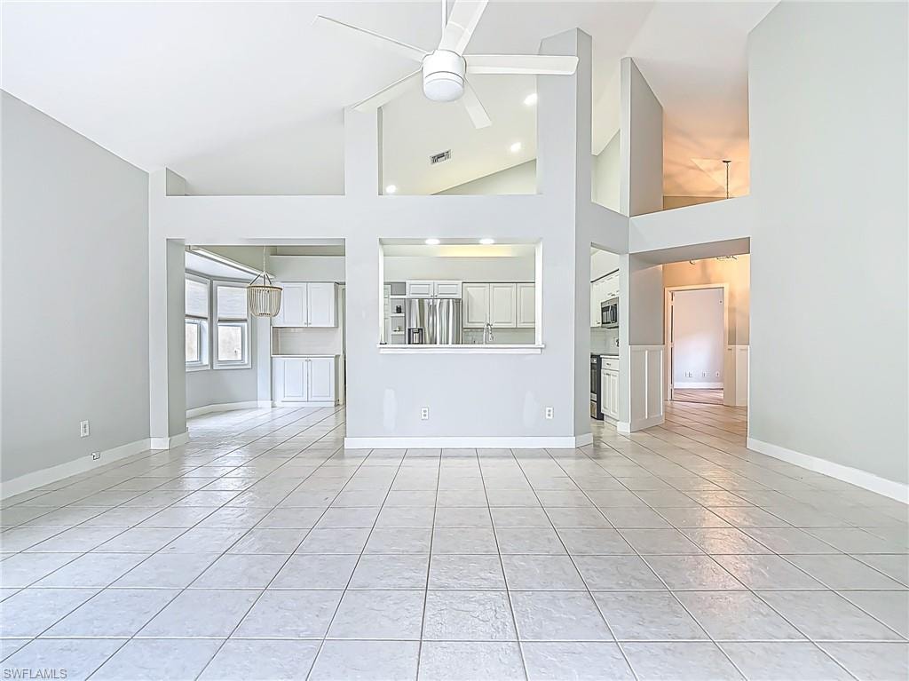 Unfurnished living room with visible vents, light tile patterned flooring, baseboards, ceiling fan, and high vaulted ceiling