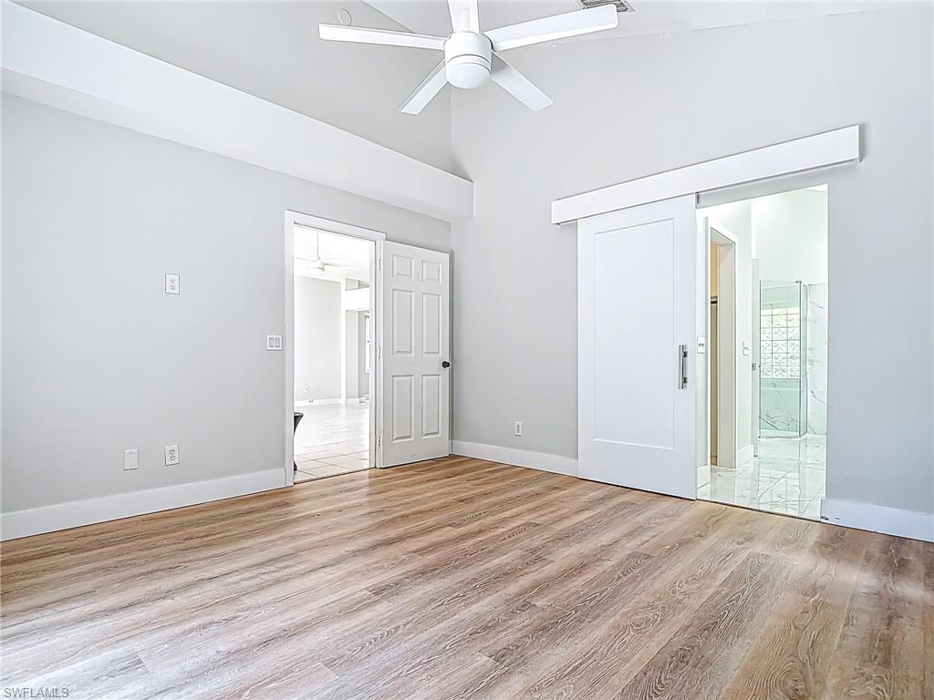 Unfurnished bedroom with baseboards, light wood finished floors, ensuite bathroom, and high vaulted ceiling
