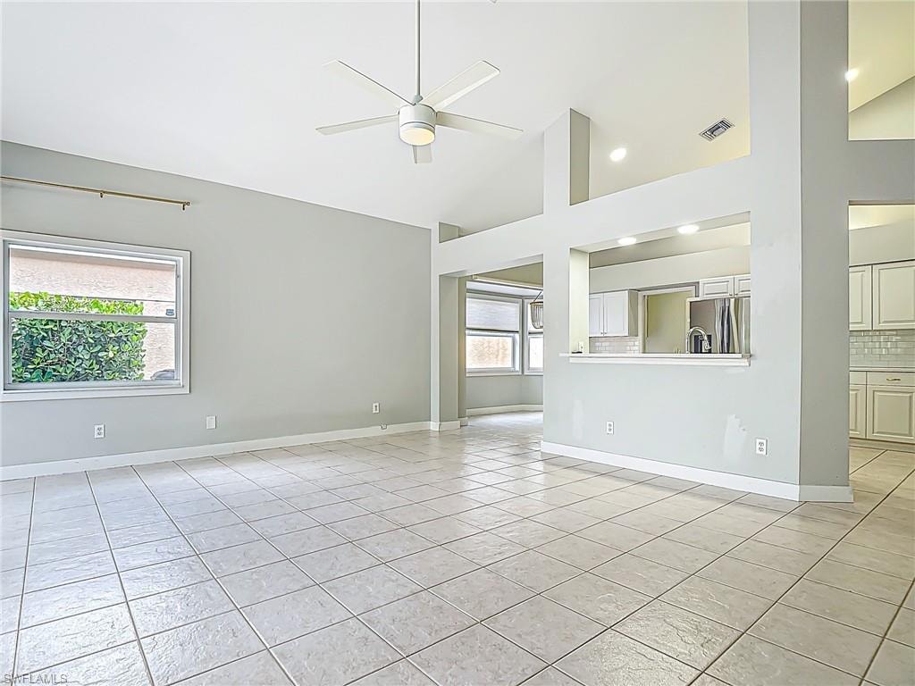 Unfurnished living room featuring ceiling fan, visible vents, light tile patterned floors, high vaulted ceiling, and baseboards