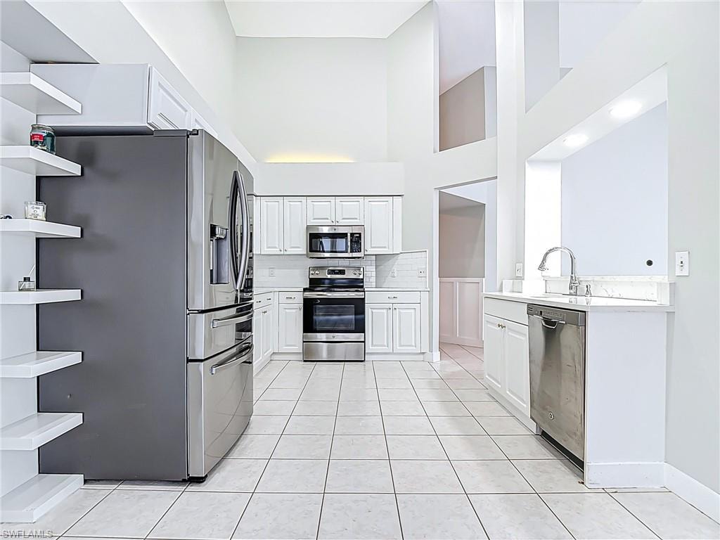 Kitchen featuring open shelves, a high ceiling, light countertops, a sink, and stainless steel appliances