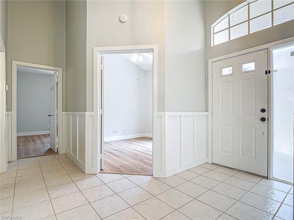 Entryway featuring a decorative wall, a high ceiling, wainscoting, and light tile patterned flooring
