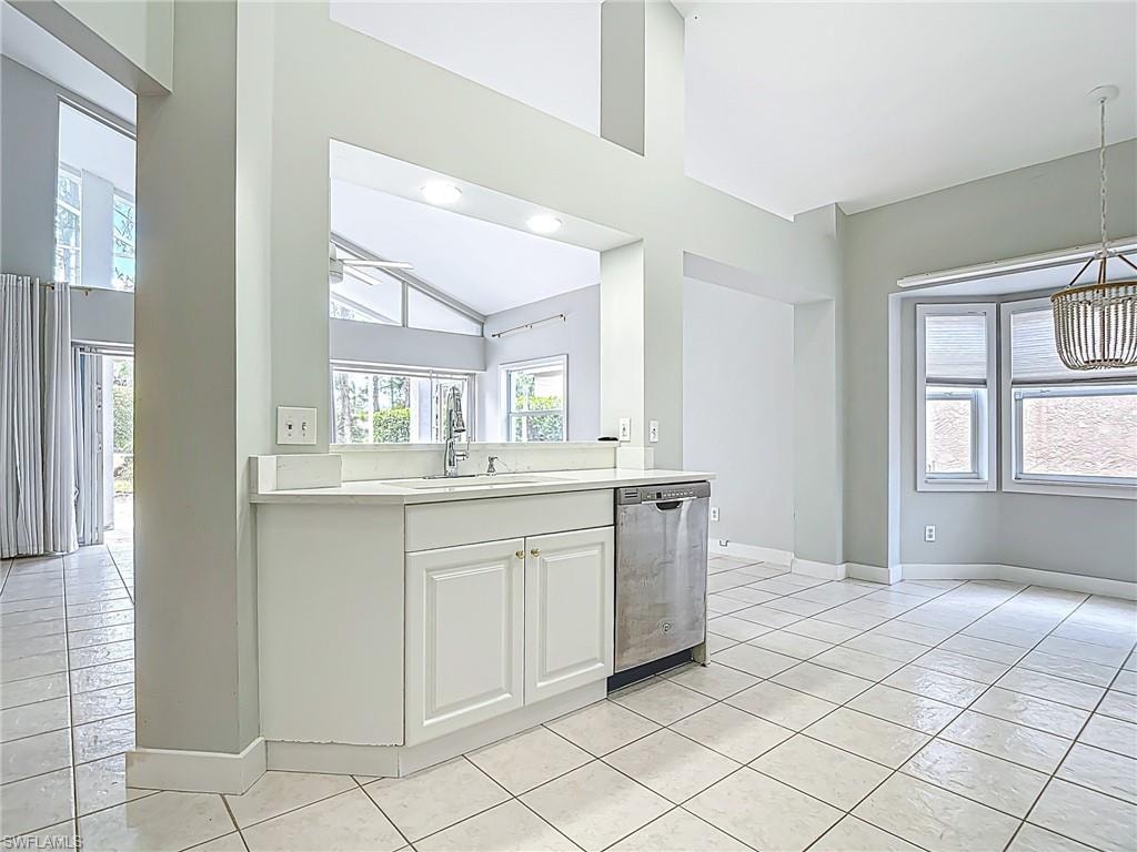 Kitchen with stainless steel dishwasher, baseboards, light countertops, white cabinets, and a sink