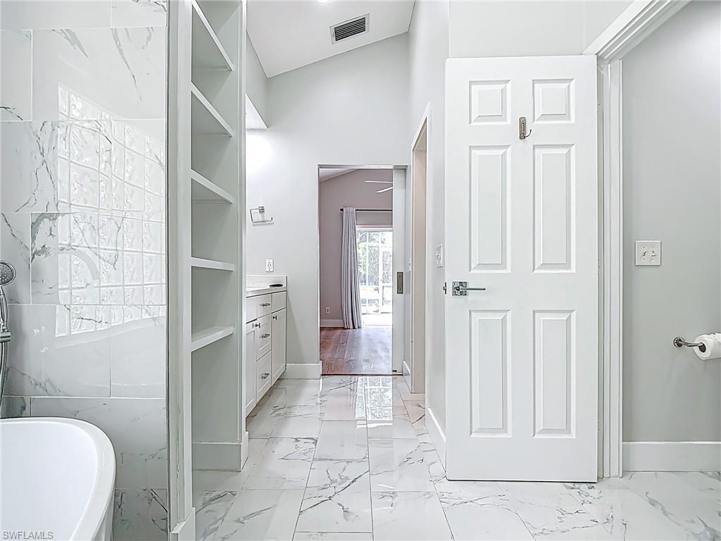 Bathroom featuring vanity, marble finish floor, a freestanding tub, baseboards, and visible vents