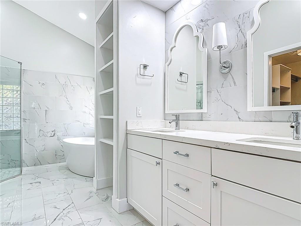 Bathroom featuring a sink, marble finish floor, a soaking tub, and tile walls