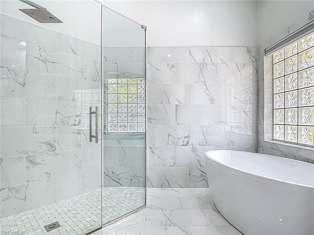 Bathroom with tile walls, plenty of natural light, a soaking tub, and a stall shower