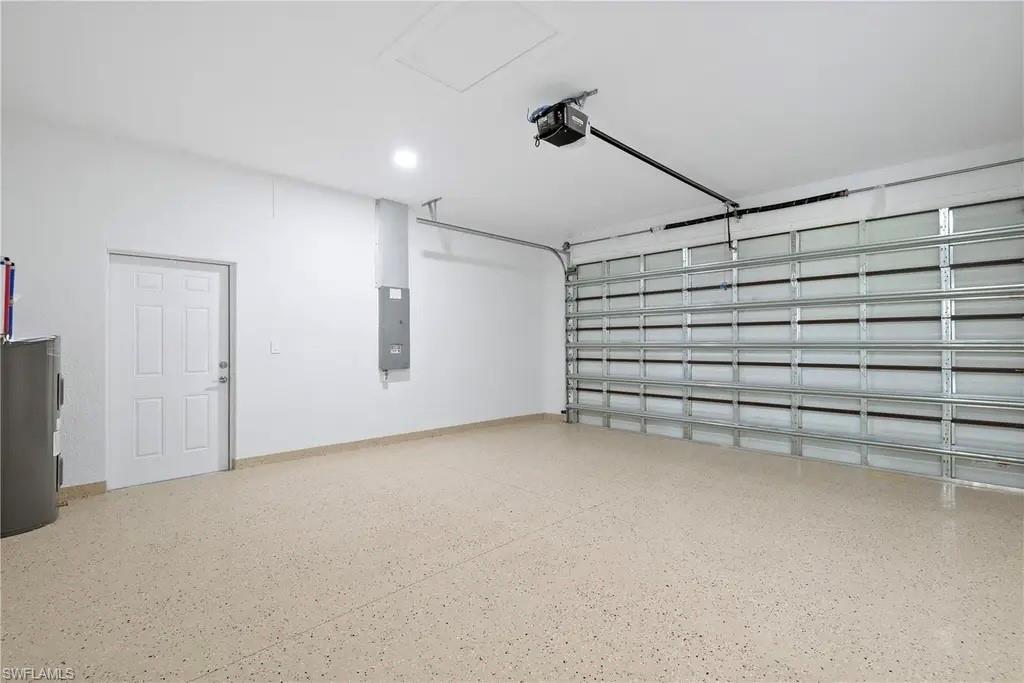 Garage featuring electric water heater, electric panel, and a garage door opener