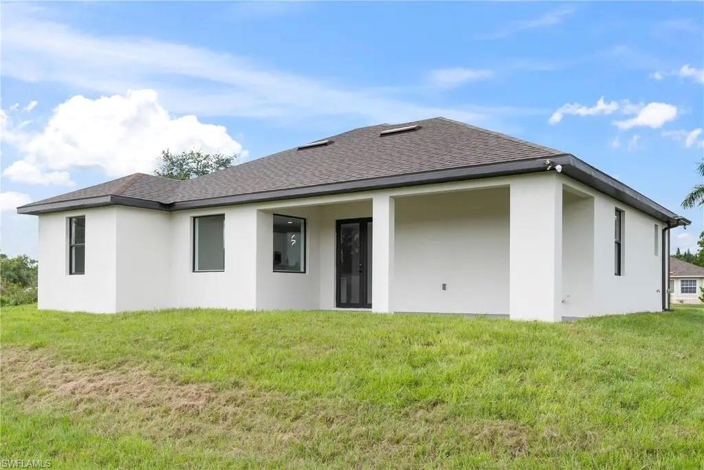 Rear view of property featuring stucco siding, a shingled roof, a yard, and a patio