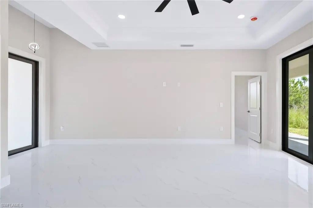 Unfurnished room featuring a tray ceiling, recessed lighting, light marble finish floors, and ceiling fan