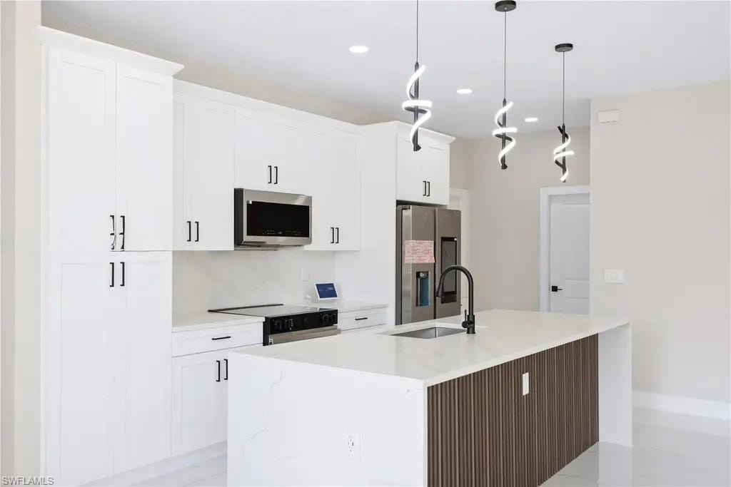 Kitchen featuring a center island with sink, stainless steel appliances, light stone counters, and white cabinetry