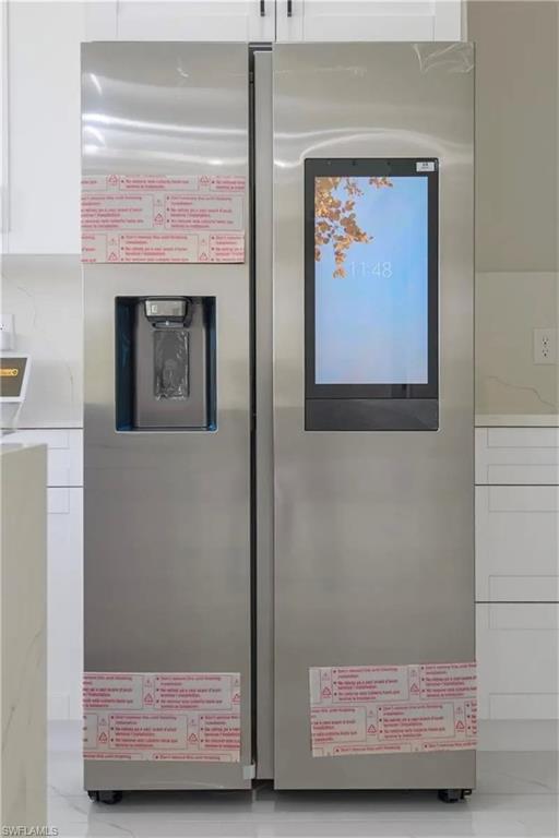 Kitchen view of stainless steel fridge, white cabinets, and light stone countertops