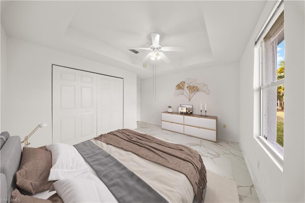 Bedroom featuring a closet, ceiling fan, a raised ceiling, and light marble finish floors