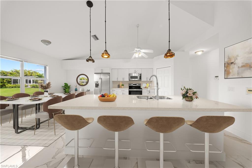 Kitchen with a kitchen bar, white cabinetry, stainless steel appliances, lofted ceiling, and decorative light fixtures