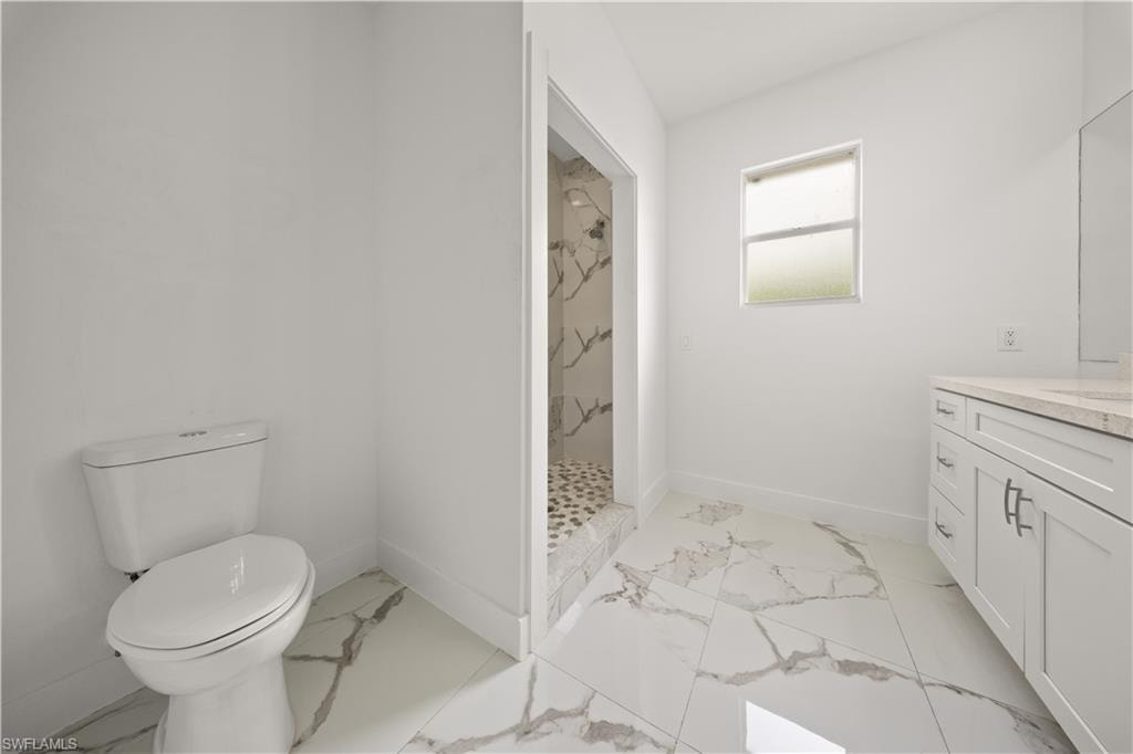 Bathroom featuring vanity, a marble finish shower, and light marble finish flooring