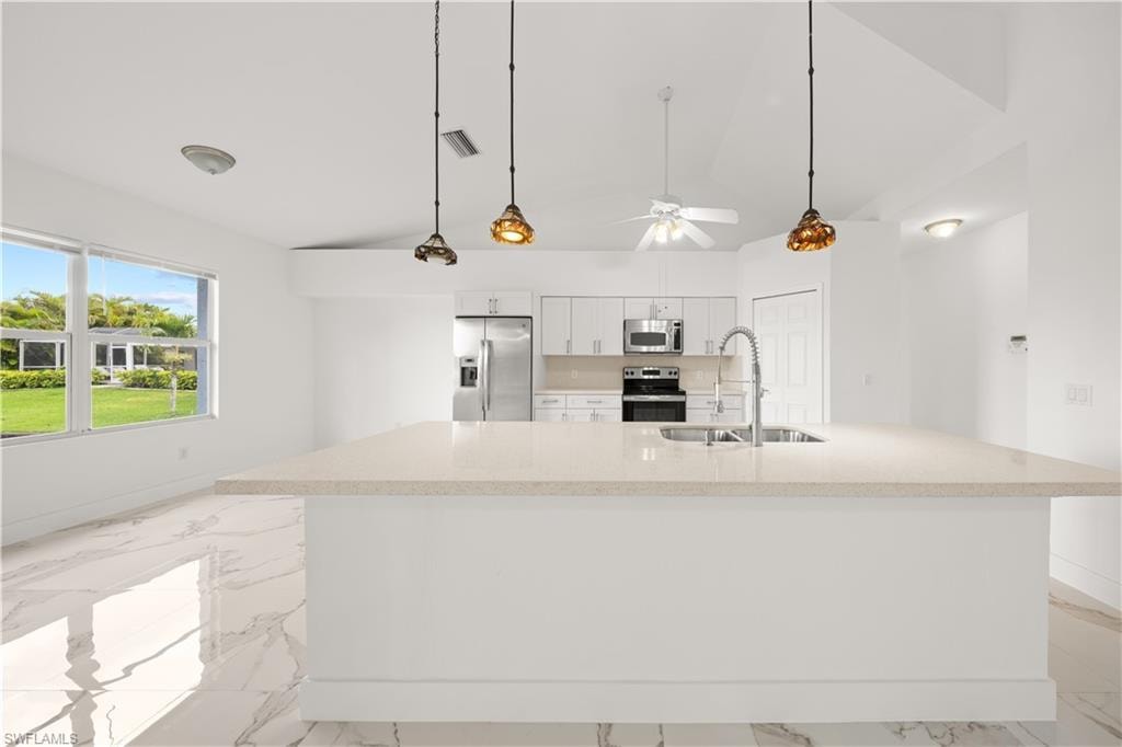 Kitchen featuring white cabinetry, stainless steel appliances, decorative light fixtures, light marble finish flooring, and lofted ceiling