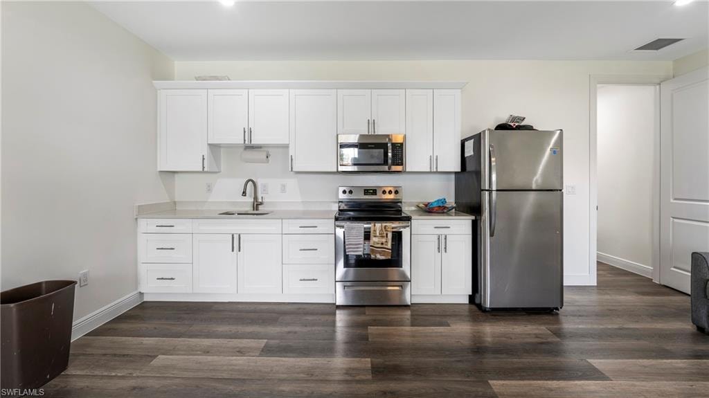 Kitchen featuring stainless steel appliances, white cabinetry, dark wood-type flooring, and light stone counters