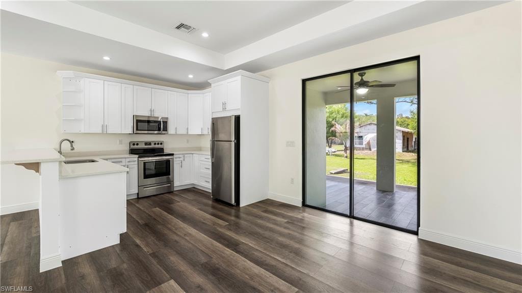Kitchen featuring open shelves, a peninsula, stainless steel appliances, white cabinets, and dark wood-style floors