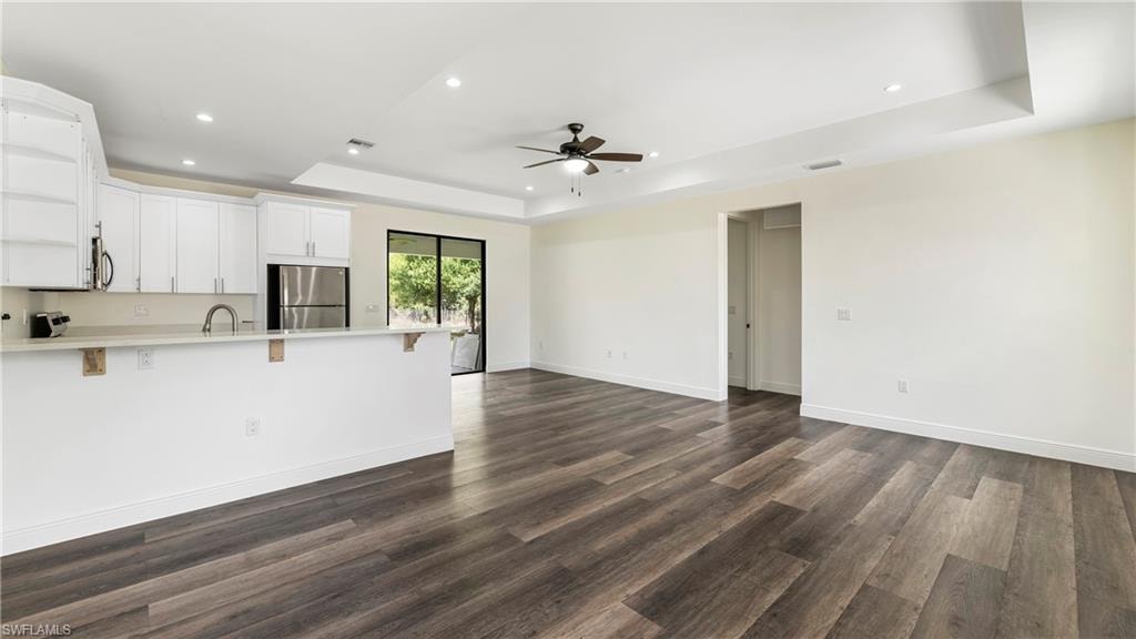 Unfurnished living room with recessed lighting, dark wood-type flooring, ceiling fan, and a tray ceiling