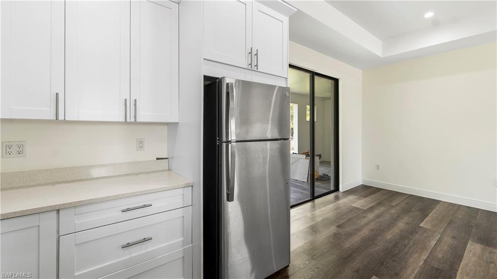 Kitchen with freestanding refrigerator, white cabinets, light stone countertops, dark wood-style flooring, and a raised ceiling