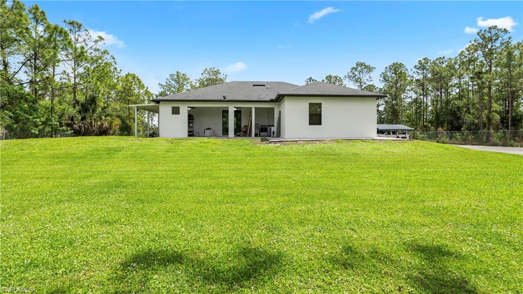 Back of house with a lawn, a patio, stucco siding, and view of scattered trees