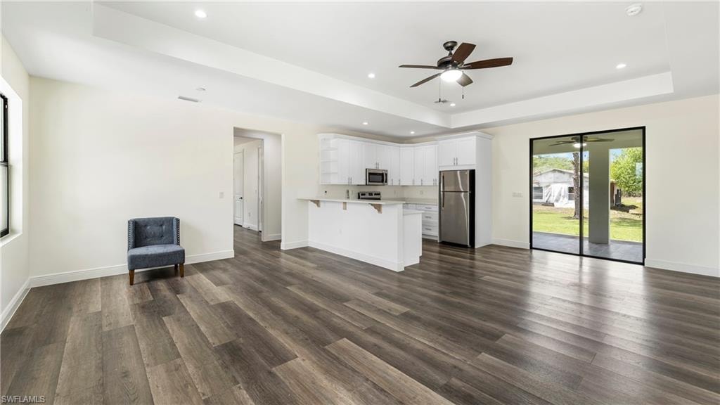 Unfurnished living room featuring a raised ceiling, a ceiling fan, dark wood-style floors, and recessed lighting