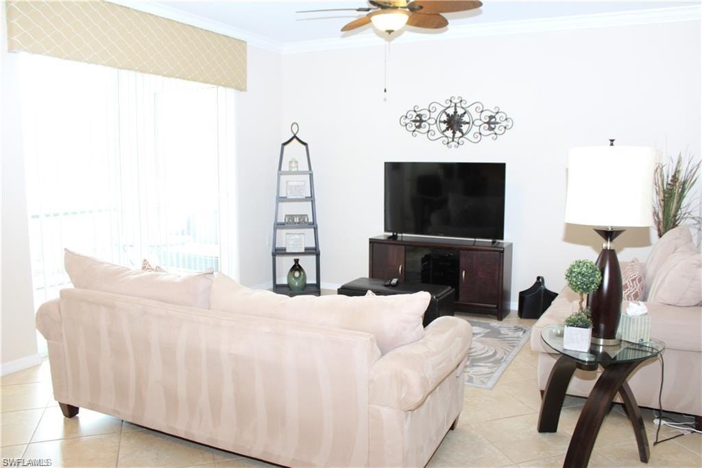 Living room with light tile patterned flooring, ceiling fan, baseboards, and crown molding