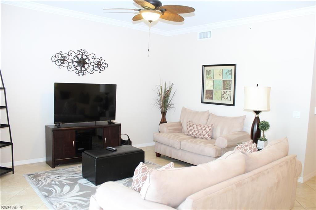 Living area with crown molding, light tile patterned floors, baseboards, ceiling fan, and visible vents
