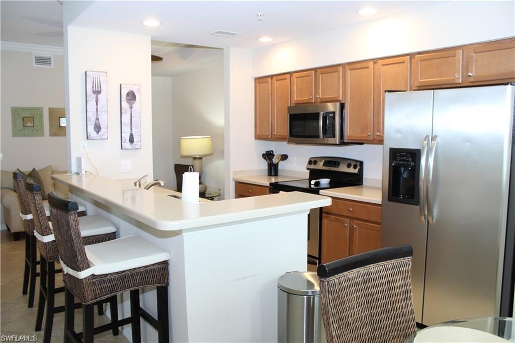 Kitchen featuring a kitchen bar, recessed lighting, stainless steel appliances, visible vents, and a peninsula