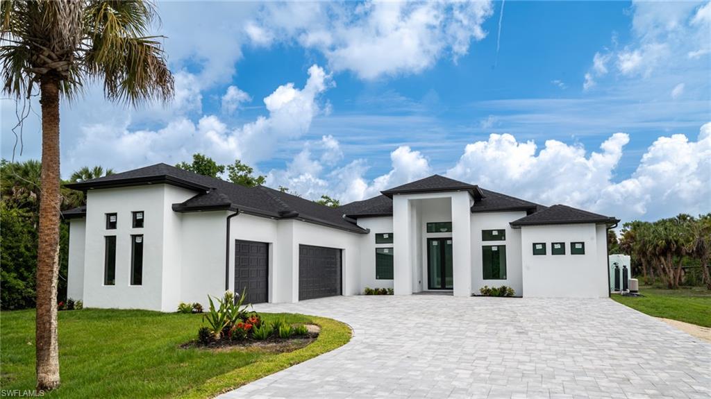 Contemporary stucco exterior featuring a two-car garage, black framed windows, a grand entrance with double doors, and a paver driveway
